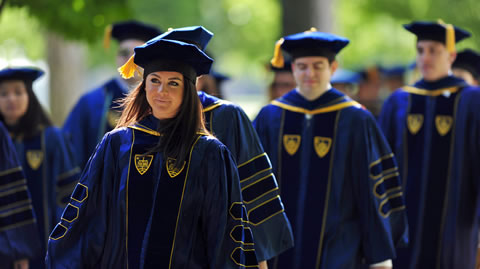 Two female and two male students wearing royal blue robes and tams