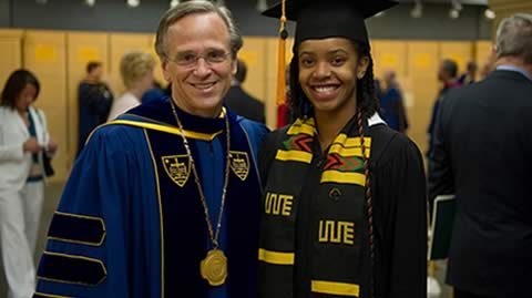 Fr. John Jenkins wearing a blue robe and the Presidential Medal posing with Katie Washington who is wearing the traditional black cap and gown