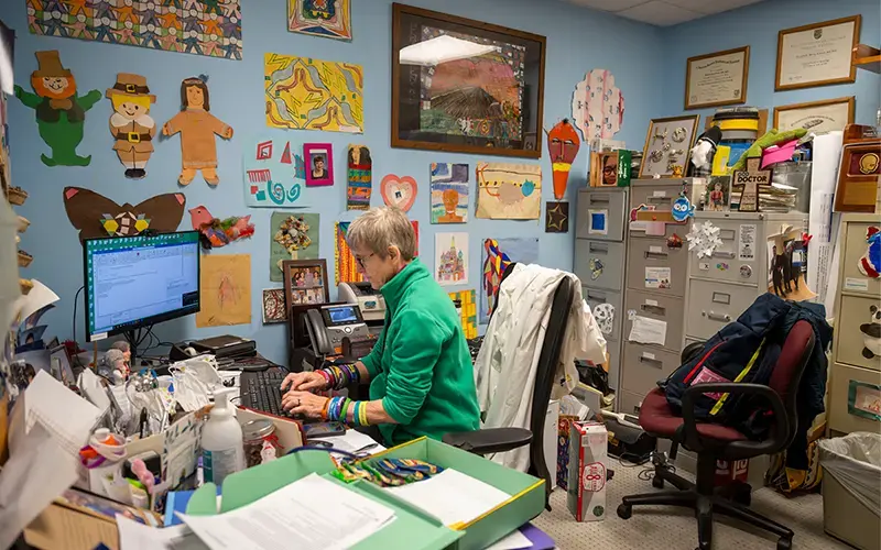 A portrait of Dr. Elizabeth Berry-Kravis sitting at her desk surrounded by colorful drawings on the walls.