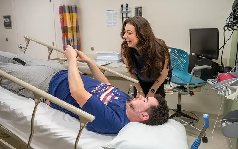 Alec Koujaian lays in the trendelenburg position, achieved by elevating the feet and legs of the patient above the level of the heart in the supine position. He's showing something on his phone to Sam Dreyer.