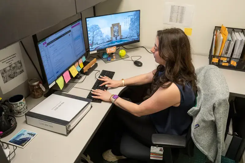 Samantha Dreyer sits at her desk looking at two computer screens. 