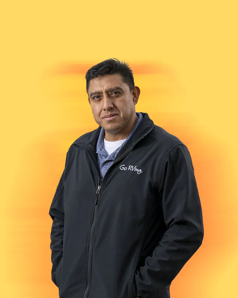 A man stands in front of a solid yellow background wearing a 'Go RVing' jacket