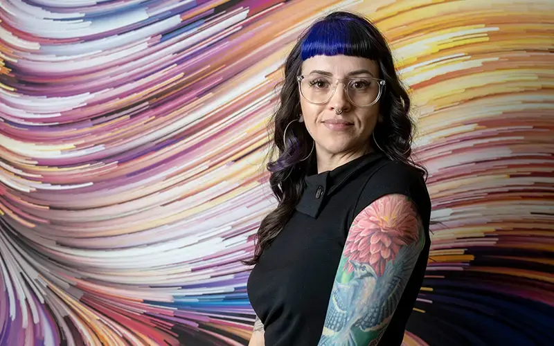 Jenny Padilla stands in front a colorful wave patterned painting.