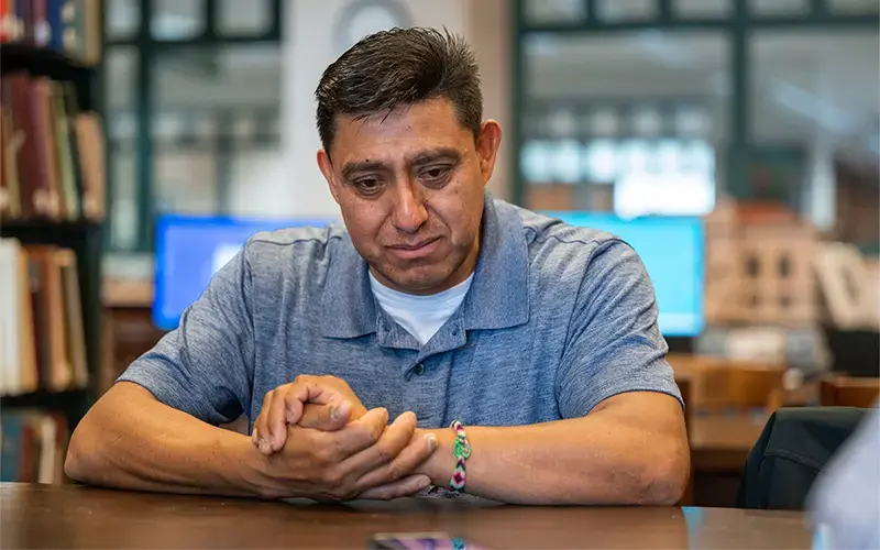 Enrique Arista Salgado sits at a table with his hands clasped. He has a sad look on his face.