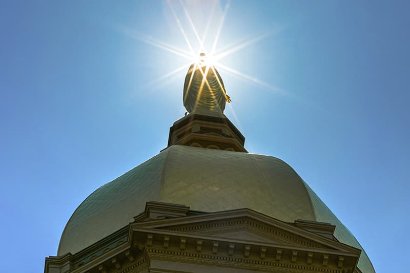A view looking up at the dome with sun rays shining through the silhouette of Mary.