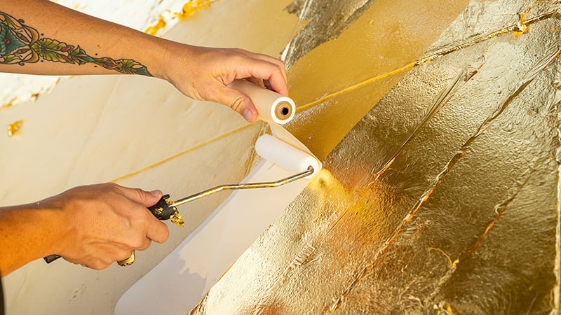 Rolls of thin gold leaf being applied to the surface of the dome with a roller.