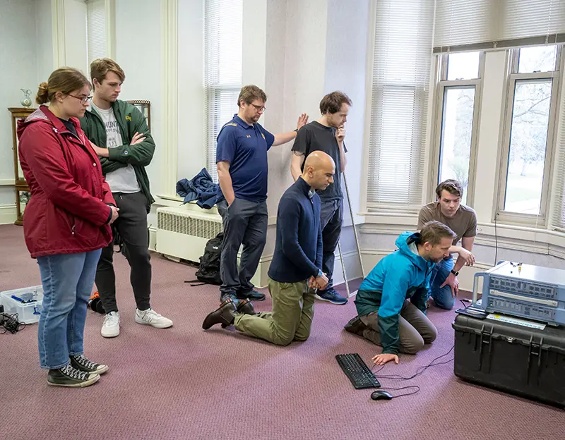 A team of researchers and students watching a spectrum analyzer inside Bertrand Hall.
