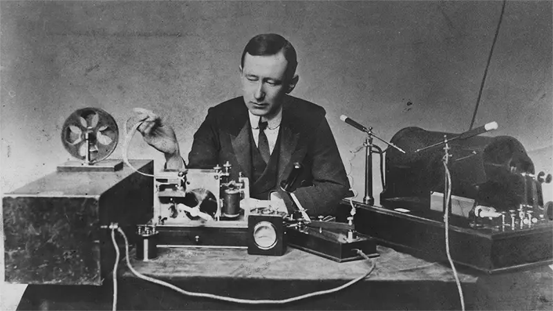 Vintage black and white photo of Guglielmo Marconi working with equipment at a workbench.