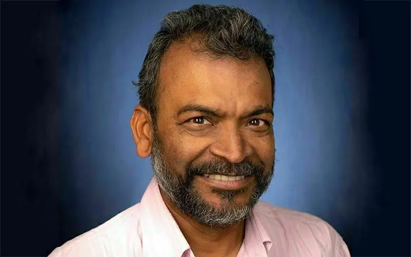 A dark-skinned man wearing a pink button-up shirt.