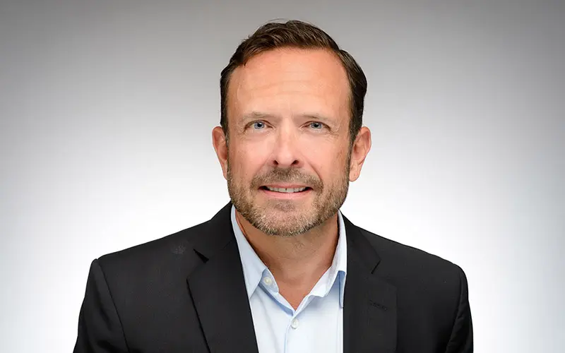 A white man wearing a light blue button-up shirt under a navy suit jacket.