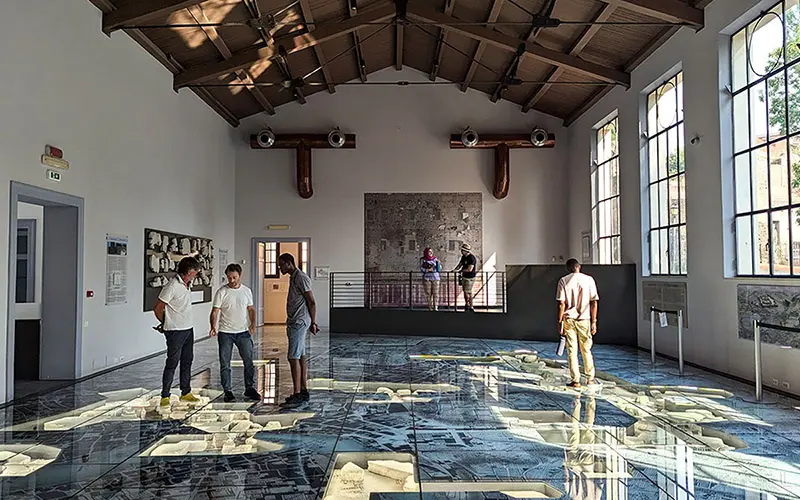 Students examine the marble map of Rome overlaid on a painting from Giovanni Battista, in a museum in Rome.