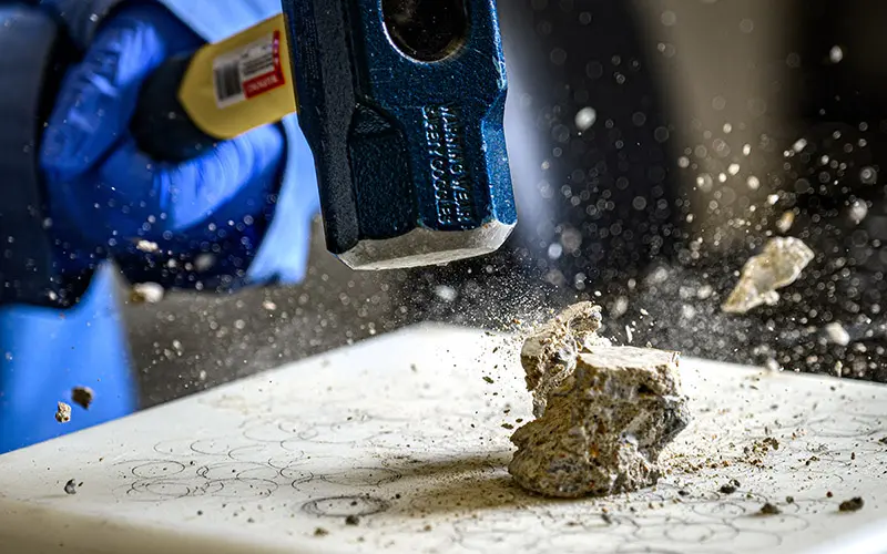 A close up picture of a rock flying into pieces after being smashed by a hammer.