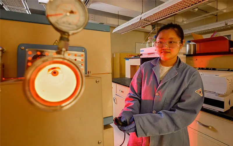 A female student operates an incinerator used for Per- and polyfluoroalkyl substances (PFAS) research in the Kyle Doudrick lab. The incinerator glows red with heat.