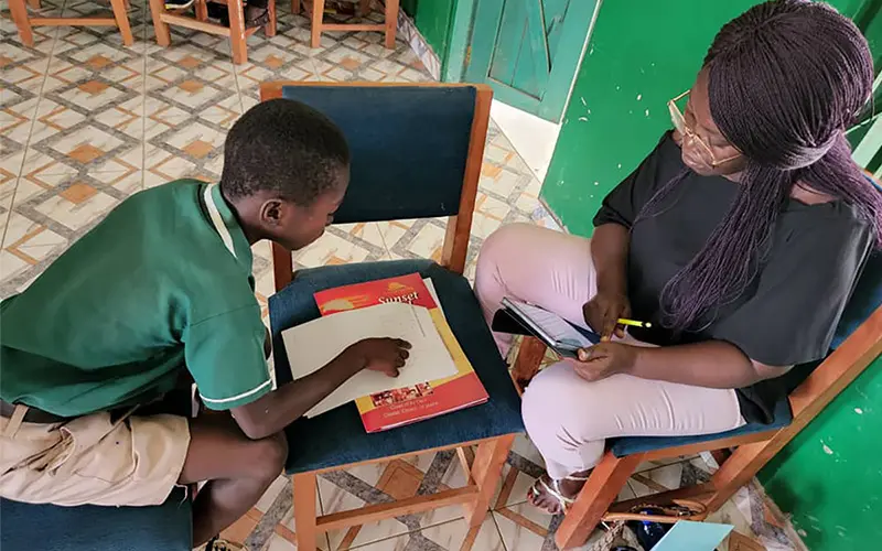 A young man and a woman are studying with their papers on the chair between them.