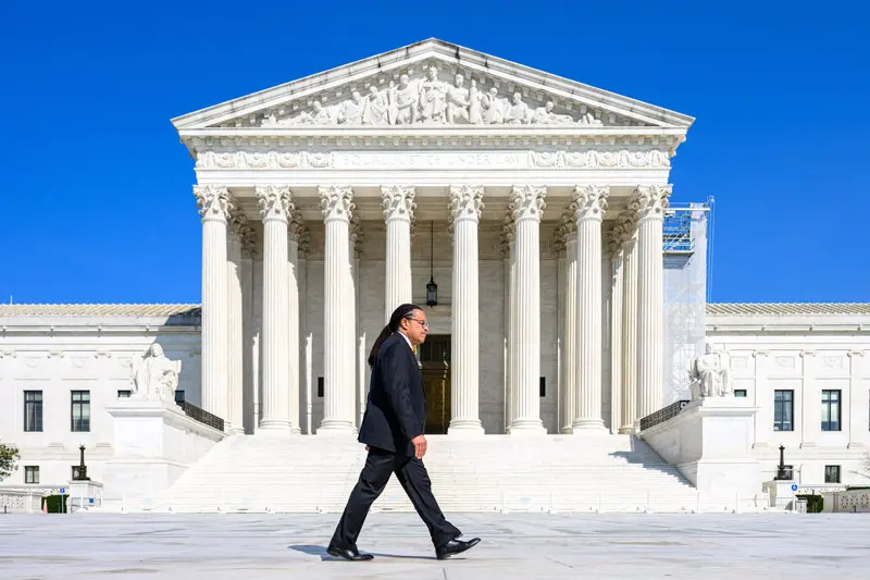 Marcu Cole, a black man, walks across the steps of the Supreme Court in Washington DC.