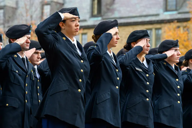 Several individuals in U.S. Army dress uniforms salute with their right hands touching their berets.