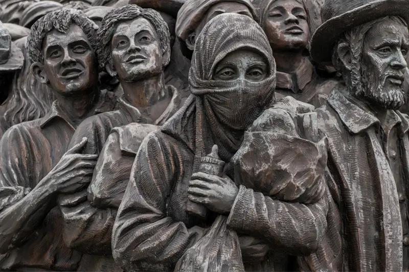 A close up of the Angels Unawares sculpture, a bronze sculpture of migrants and refugees from various lands crowded on a 20-foot boat at the Catholic University of America in Washington, DC.