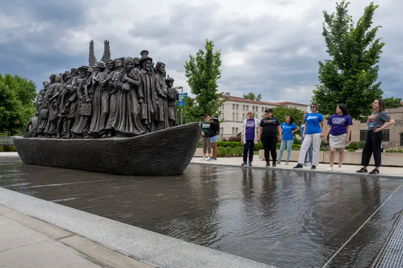 A group of teachers observe the Angels Unawares sculpture, a bronze sculpture of migrants and refugees from various lands crowded on a 20-foot boat at the Catholic University of America in Washington, DC.