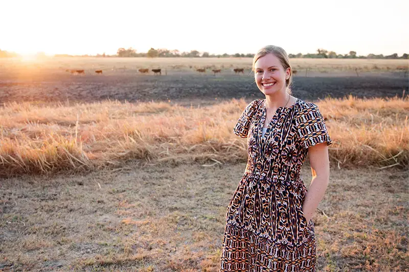 Grace Clinton standing in a fallow field with livestock in the far distance.