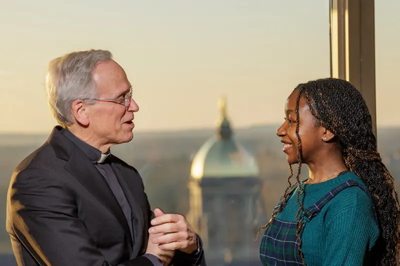 Joy Agwau talks to Fr. Jenkins. The Golden Dome is in the background. 