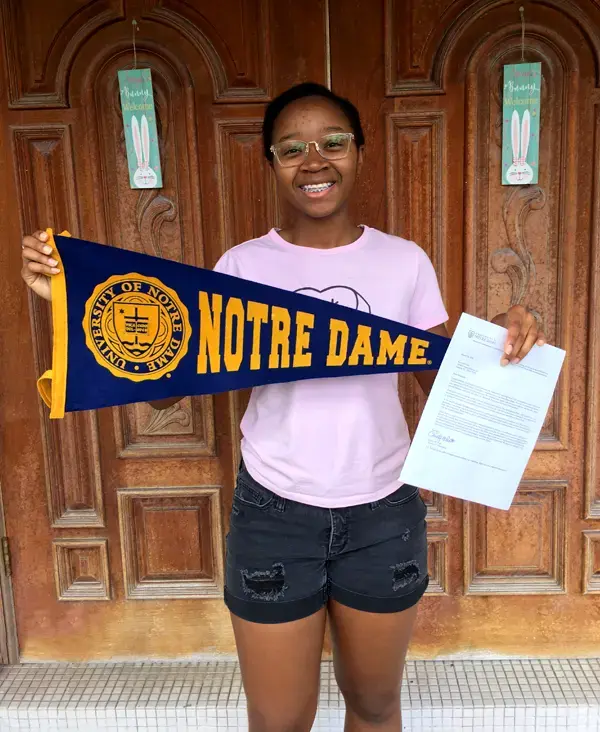 Savannah Carr stands in front of a wood door holding a pennant with the words Notre Dame on it.