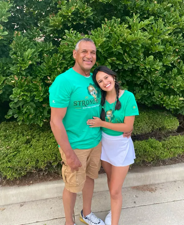 Elizabeth Gonzalez and her father wearing green, standing in front of some bushes.