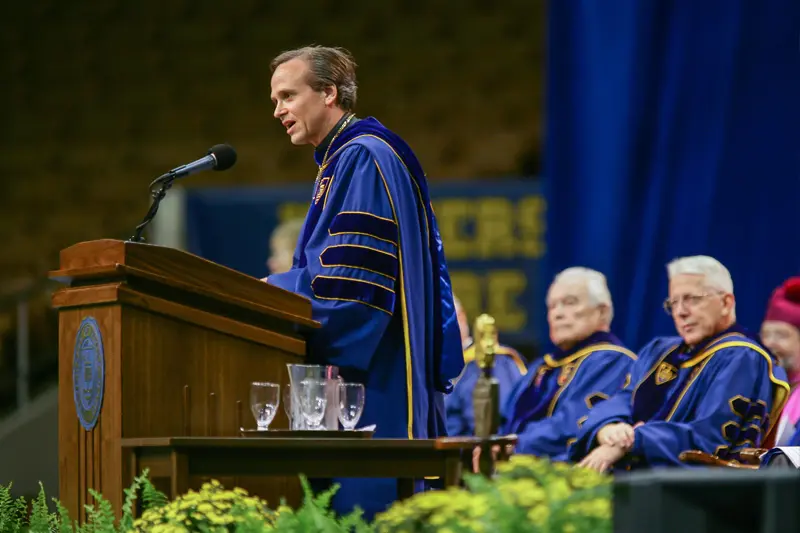 Fr. Jenkins stands at a podium in his academic robes.