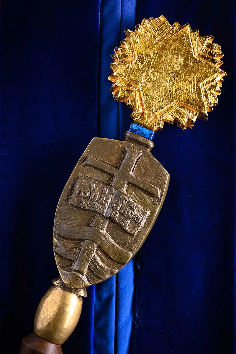 A close up of the University Mace features a bronze shield inscribed with University of Notre Dame du Lac 1842 below a golden burst of stars