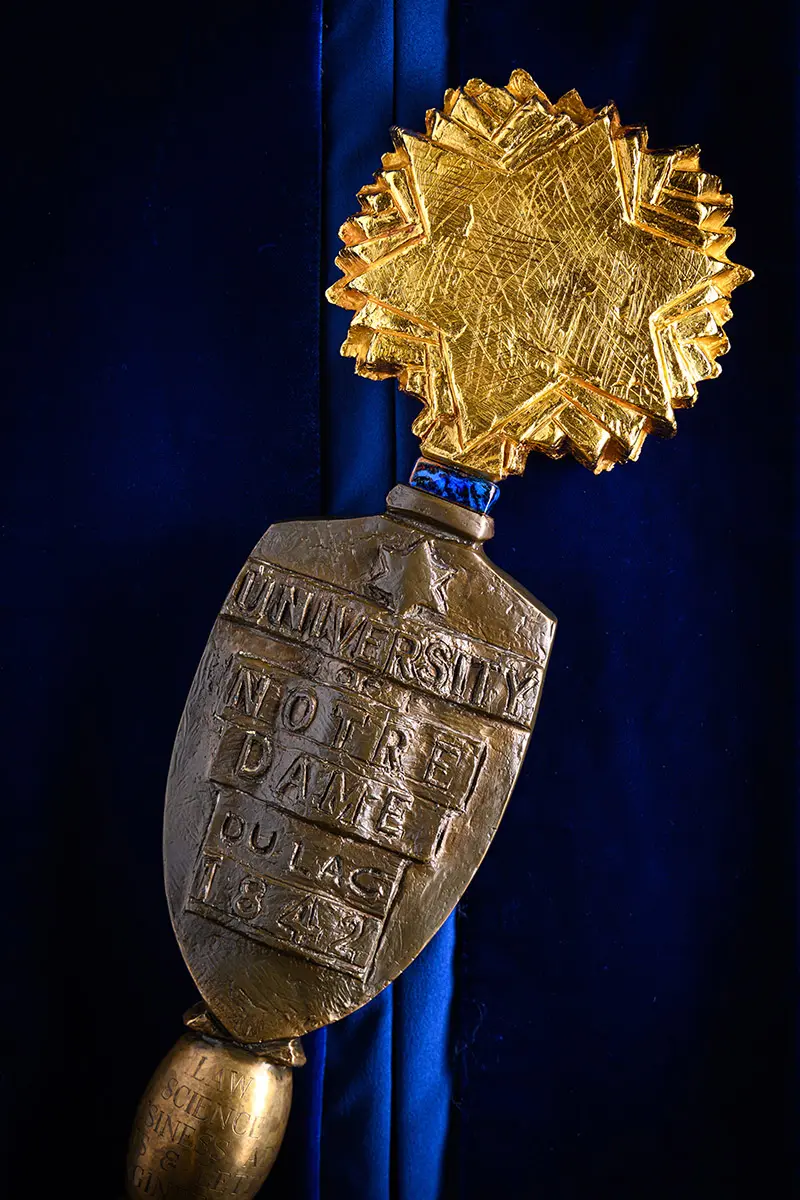 A close up of the University Mace features a bronze shield inscribed with University of Notre Dame seal below a golden burst of stars