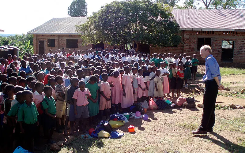 Fr. Bob Dowd stands in front of a large group of black children outside a brick building.