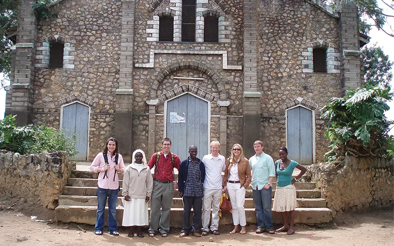 Father Bob Dowd stands in front of a gray brick building with seven other people.