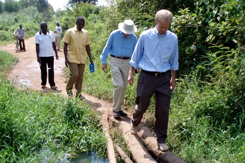 Father Bob Dowd walking on a log over a creek with a group of people in line behind him.