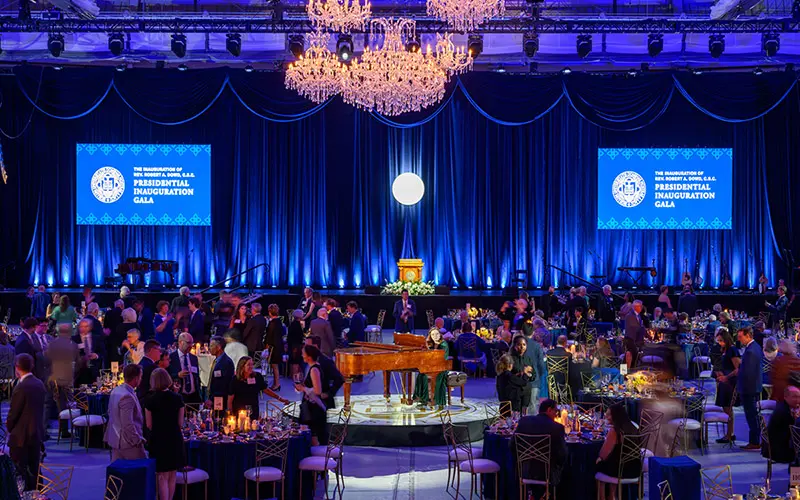 A wide shot of Miriam Rice sitting at the piano in the middle of tables filled with people.