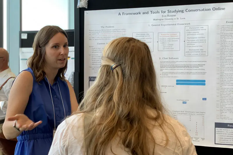 Erin Rossiter stands in front of a presentation board talking to another woman.