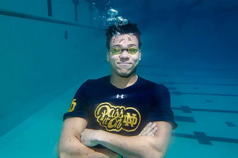 A college student wearing goggles crosses his arms and floats under water.