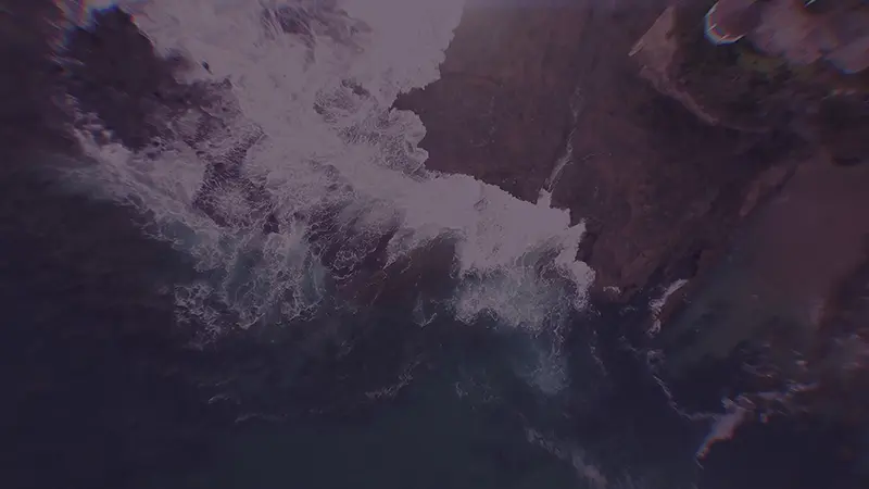 Aerial view of waves crashing down onto shore in slow motion.