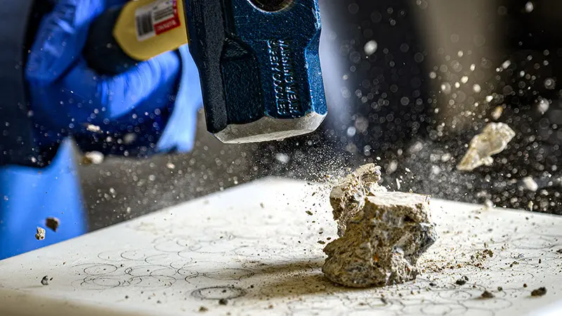 A close up picture of a rock flying into pieces after being smashed by a hammer.