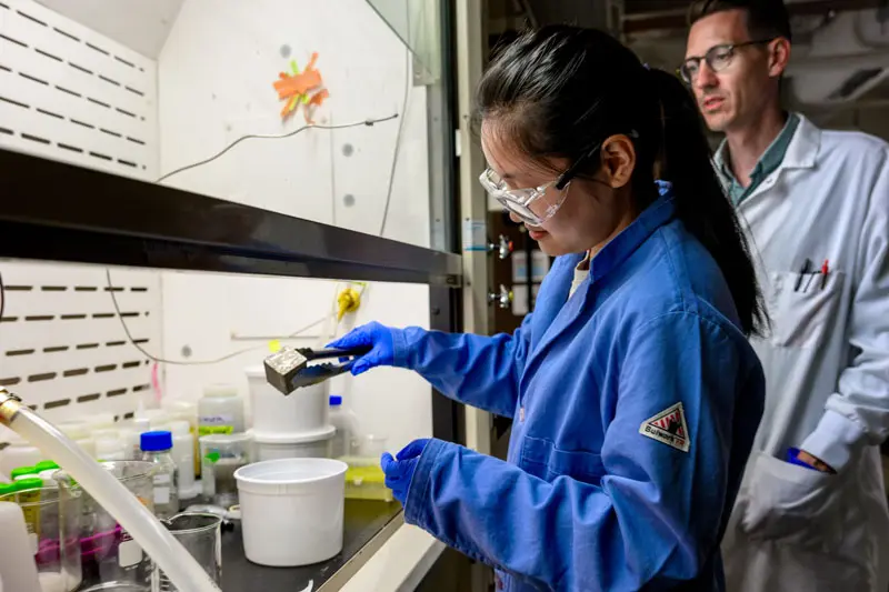 A student putting cement samples in a solution while Kyle Doudrick oversees the process.