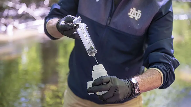 Gary Lamberti collecting water with a syringe while standing in a creek.