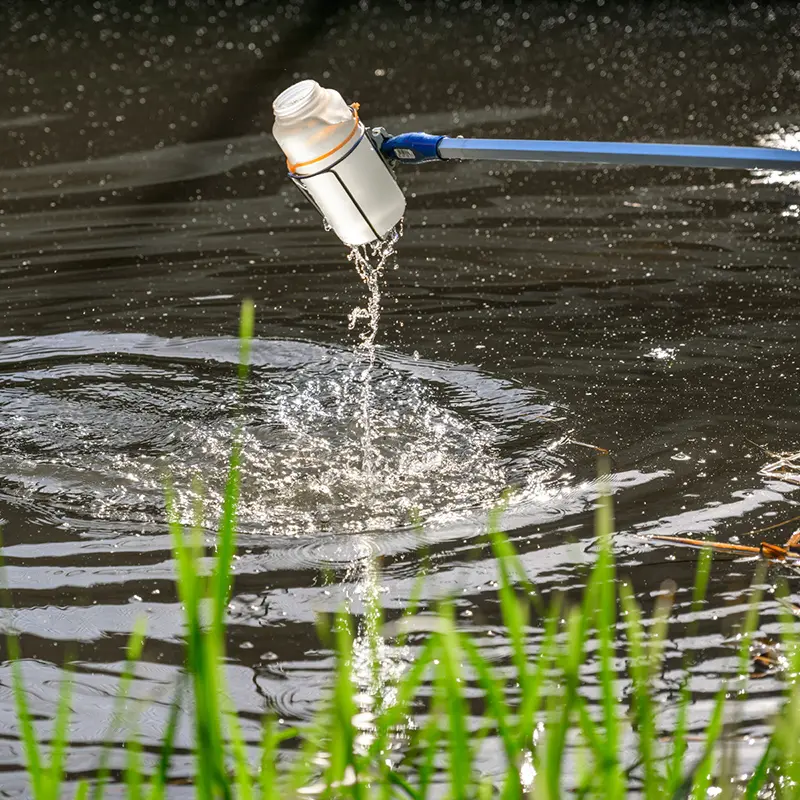 A cup on a pole is taking samples of water out of the river.