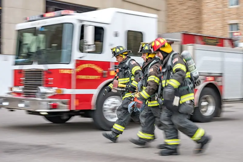 Three firefighters in full gear walking by a parked firetruck