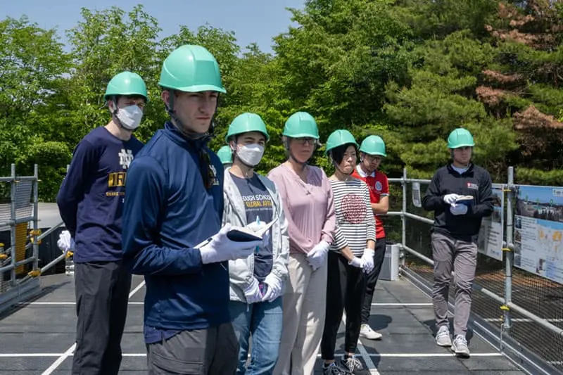 While wearing hardhats, the Notre Dame team listens as a TEPCO representative explains the layout of the nuclear plant and the events that led to the meltdown.