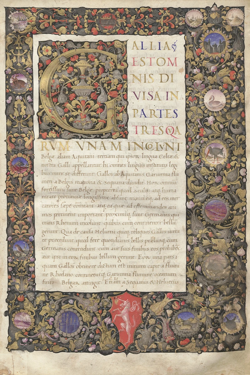 An illuminated manuscript page with elaborate floral borders and a large, gold-embellished letter 'G.' The borders contain small illustrations of animals, landscapes, and crests. Latin text begins below the illuminated letter. A white unicorn on a red shield is situated at the bottom center.