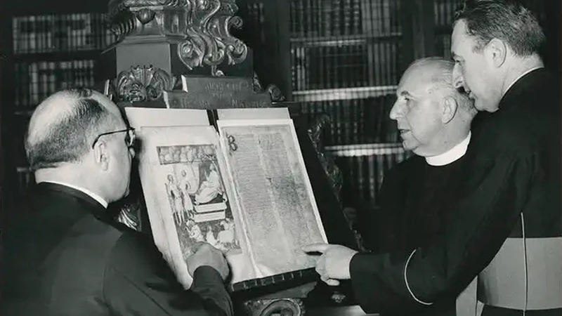 A black and white archive photograph showing 3 white men pointing to an old manuscript.