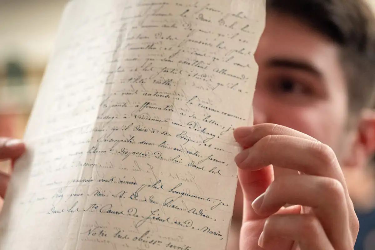 A student holds up a piece of paper with calligraphic writing on both sides of it up to the light.