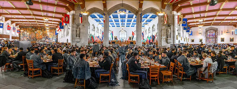 A panoramic view of the West Point mess hall filled with soldiers in their uniforms sitting down at tables.