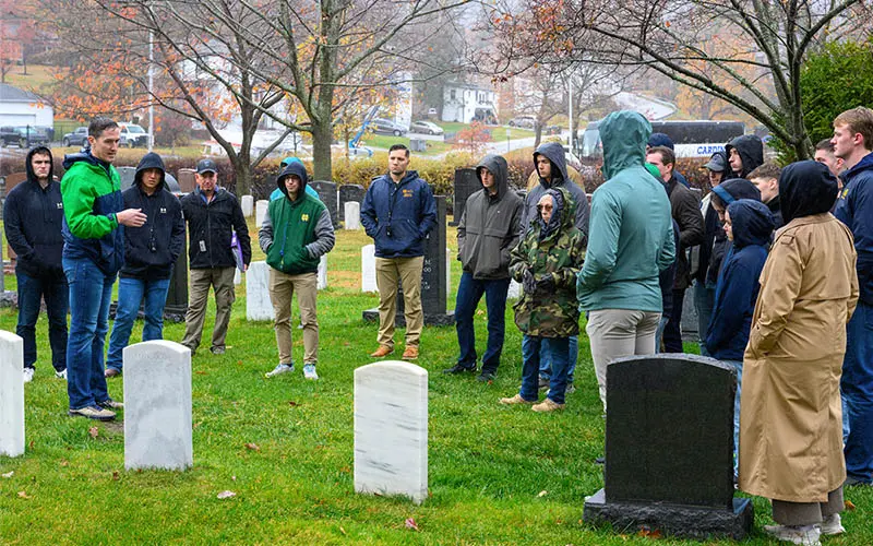 A group of cadets stand around gravestones at West Point Cemetery, where gravestones mark the final resting place of famous military people from George Custer to Norman Schwartzkopf.