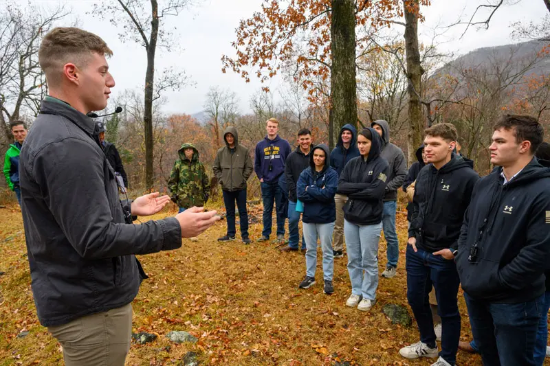 A white man stands with his hands out talking to a group of cadets near the Trail of the Fallen, near West Point, in New York. 