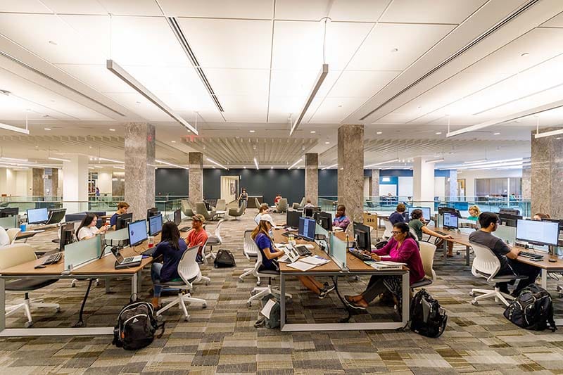 Students study at long tables with computers.