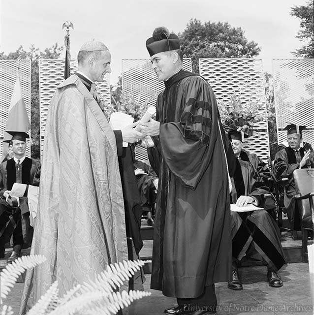 Father Hesburgh, dressed in graduation regalia, hands an honorary degree to Cardinal Montini, dressed in vestements, on the stage during Commencement.